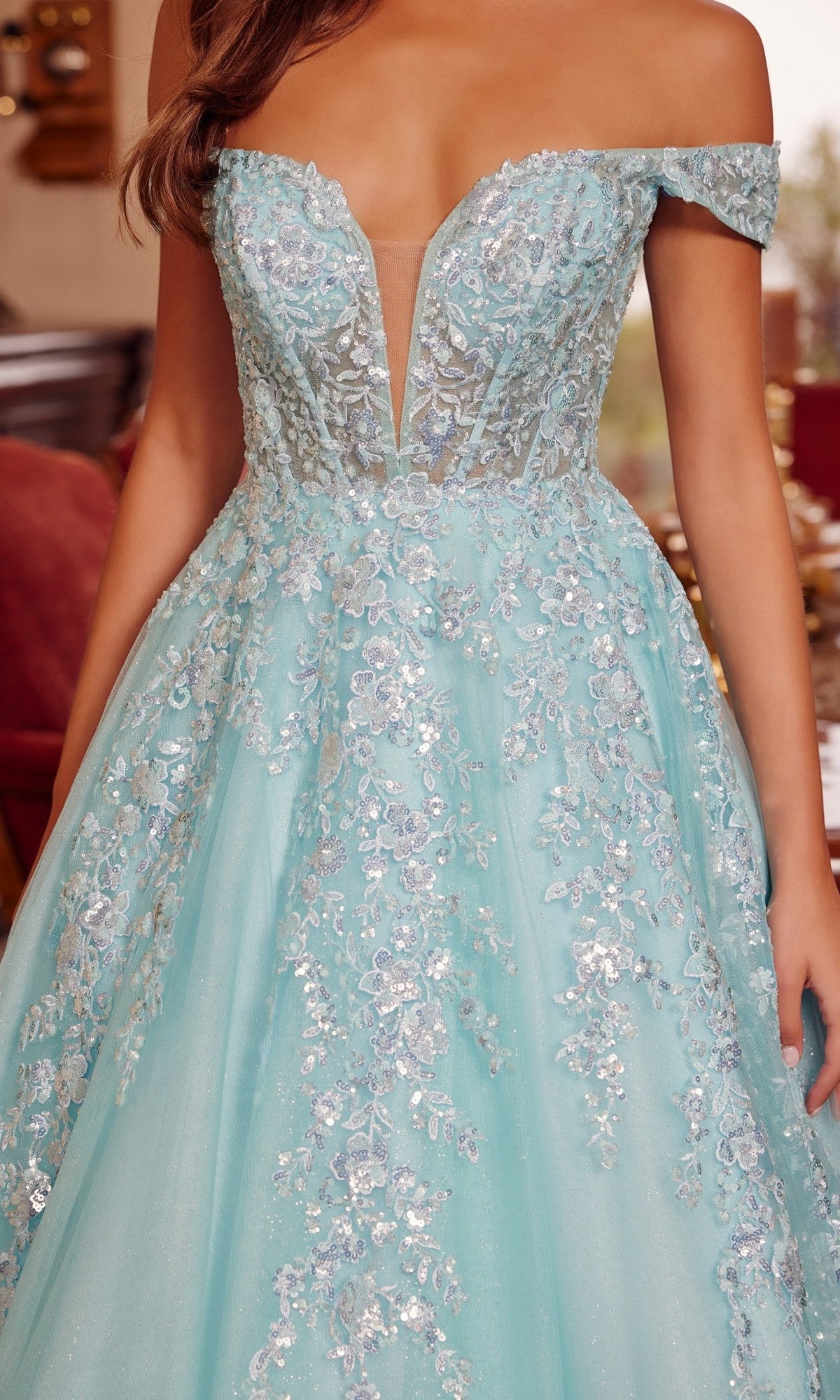 A woman wears the Nox Anabel H1881 long prom dress, an off-the-shoulder light blue tulle ball gown with silver floral embroidery and a sheer deep V neckline.